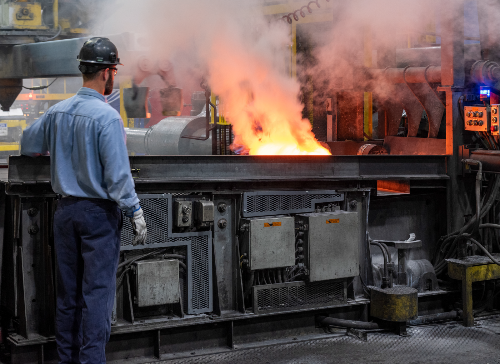 Industrial worker standing beside a furnace with molten metal and flames visible