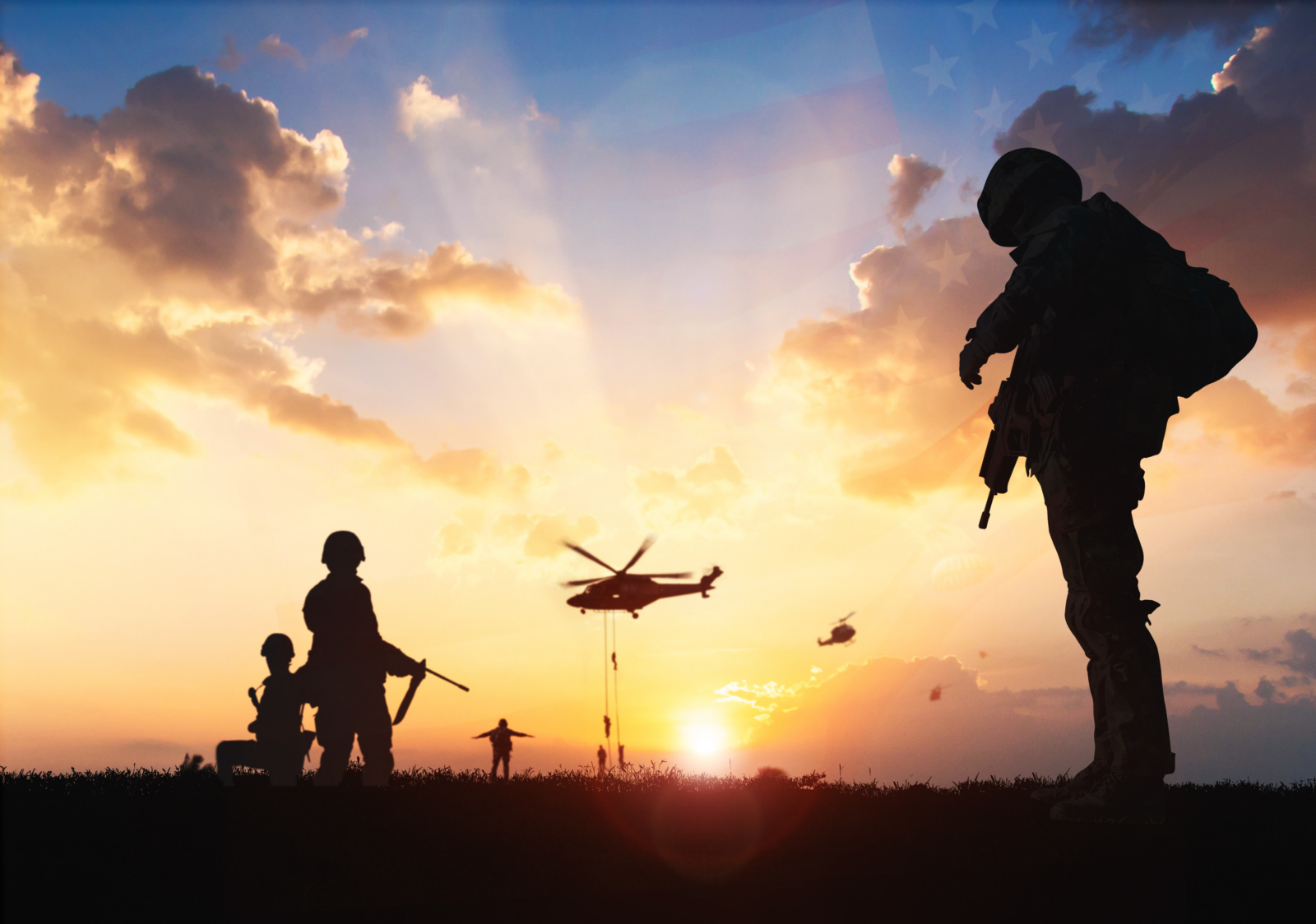 Silhouetted soldiers on the ground with helicopters flying overhead at sunset