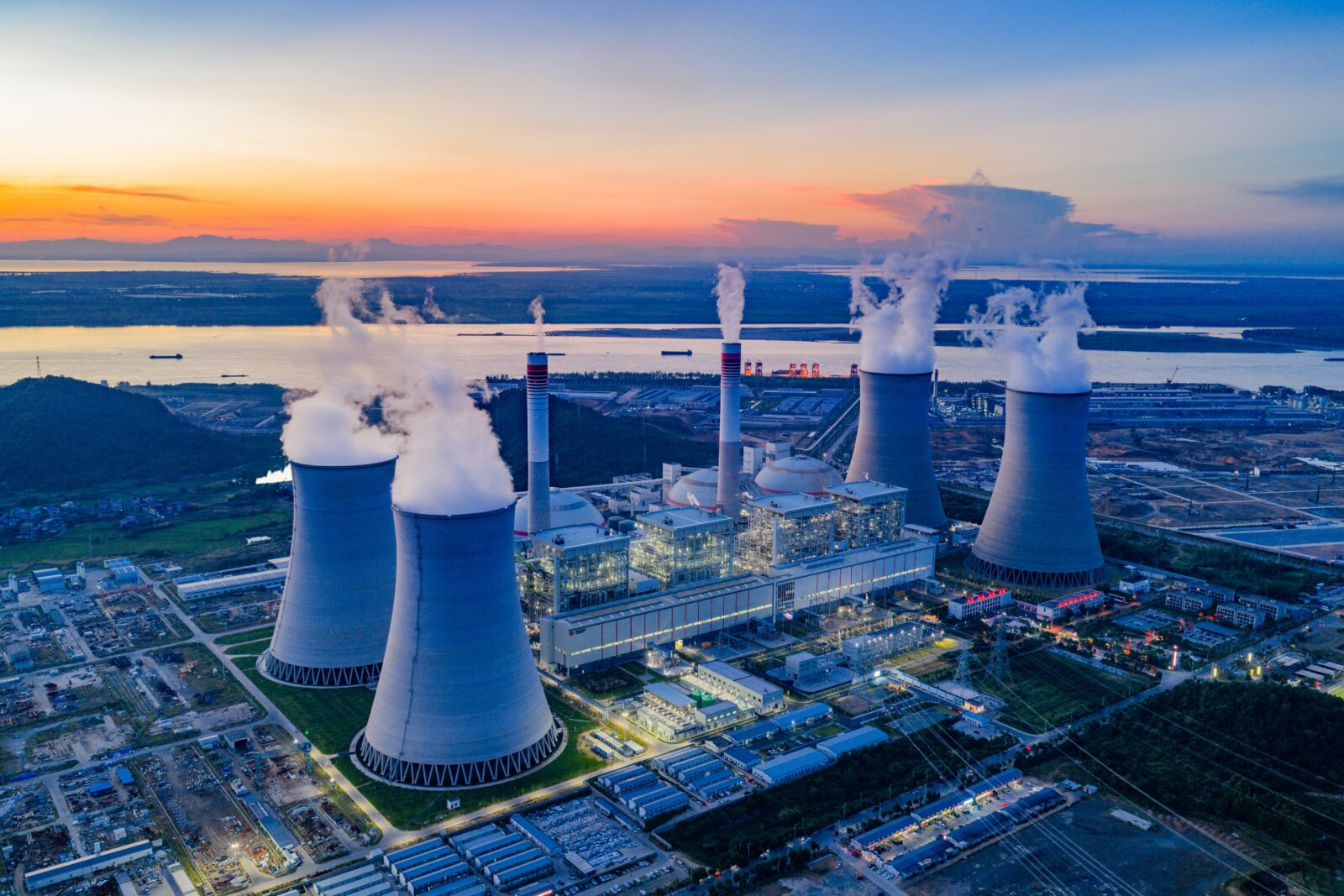 Aerial view of a power plant complex with multiple cooling towers releasing steam at sunset