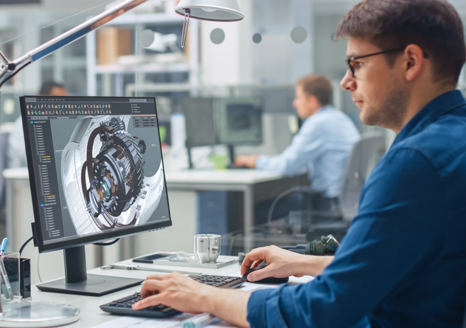 Engineer working at a computer displaying a 3D model of a mechanical assembly