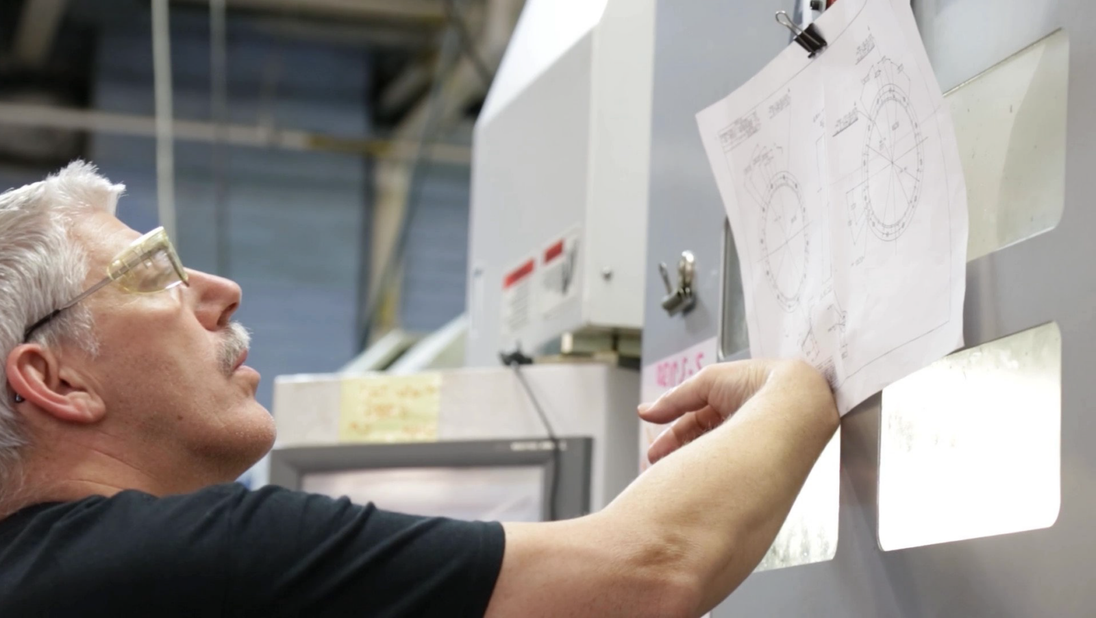 Worker referencing technical drawings mounted on an industrial machine
