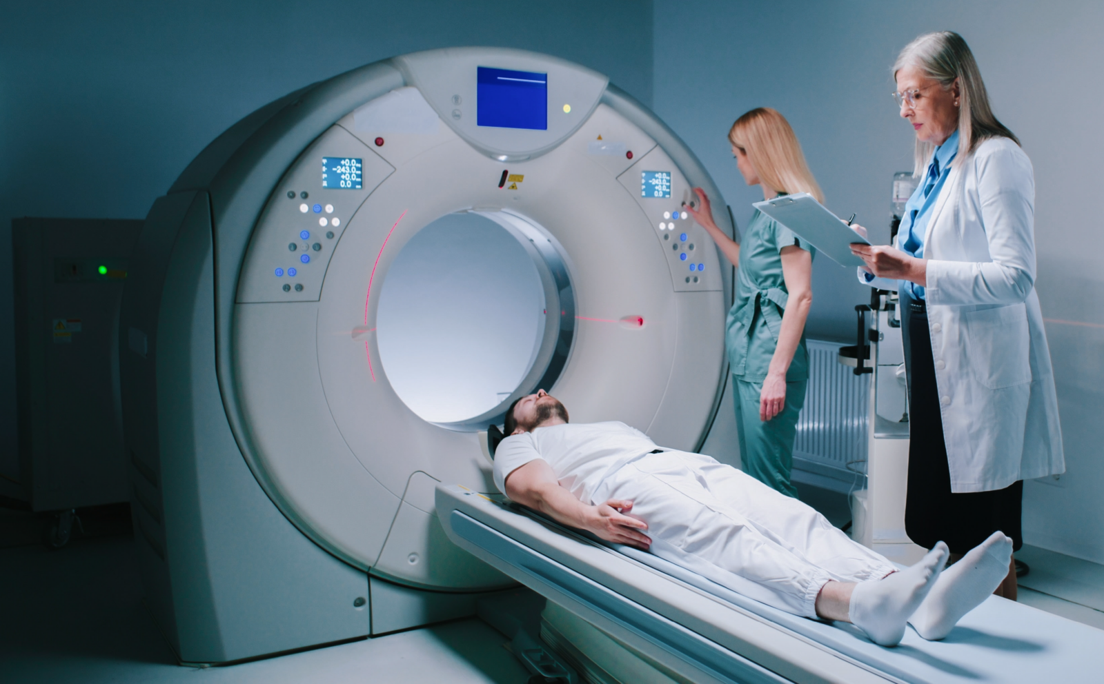 Patient positioned on a sliding table entering a medical imaging scanner with clinicians nearby