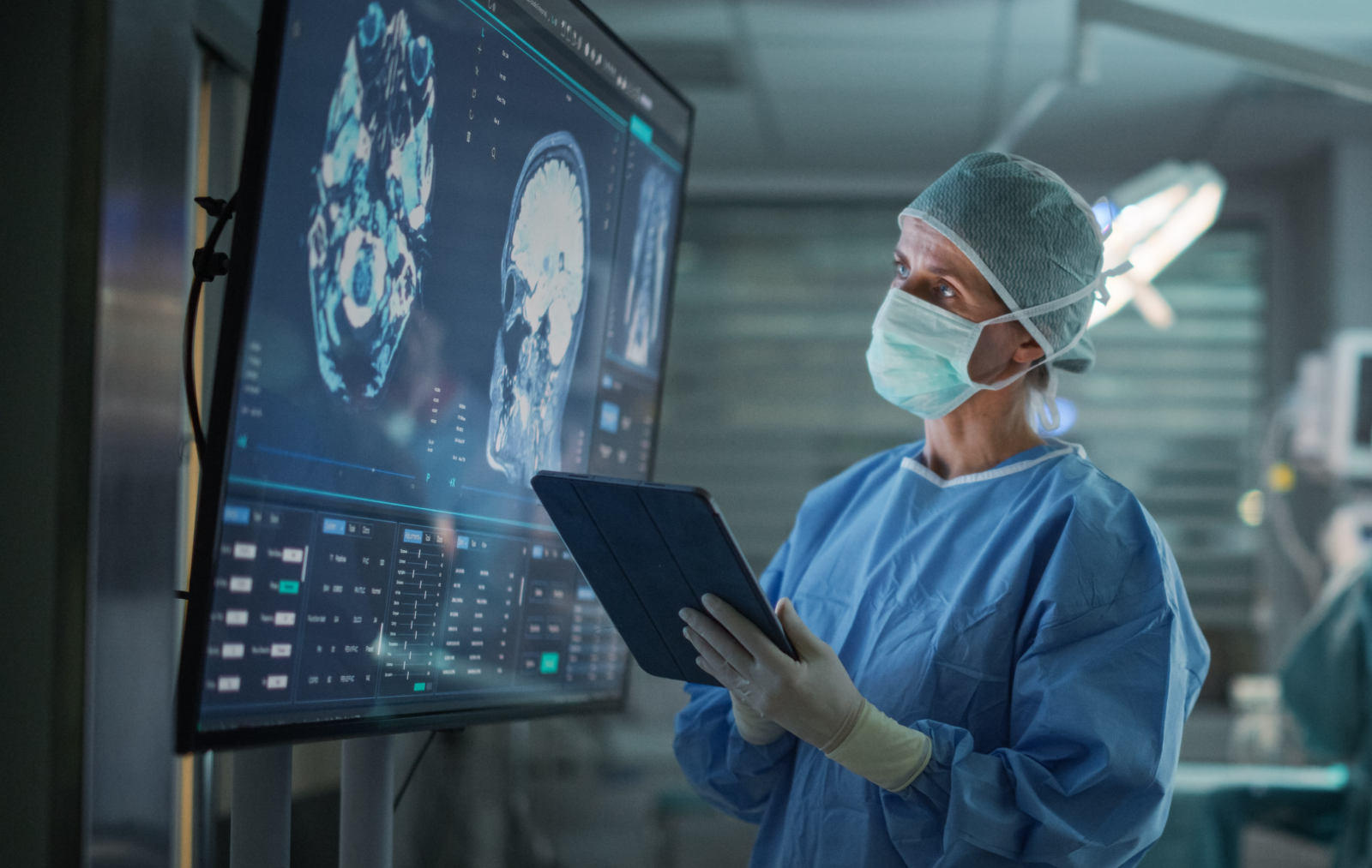 Medical professional reviewing brain imaging displayed on a large monitor while holding a tablet