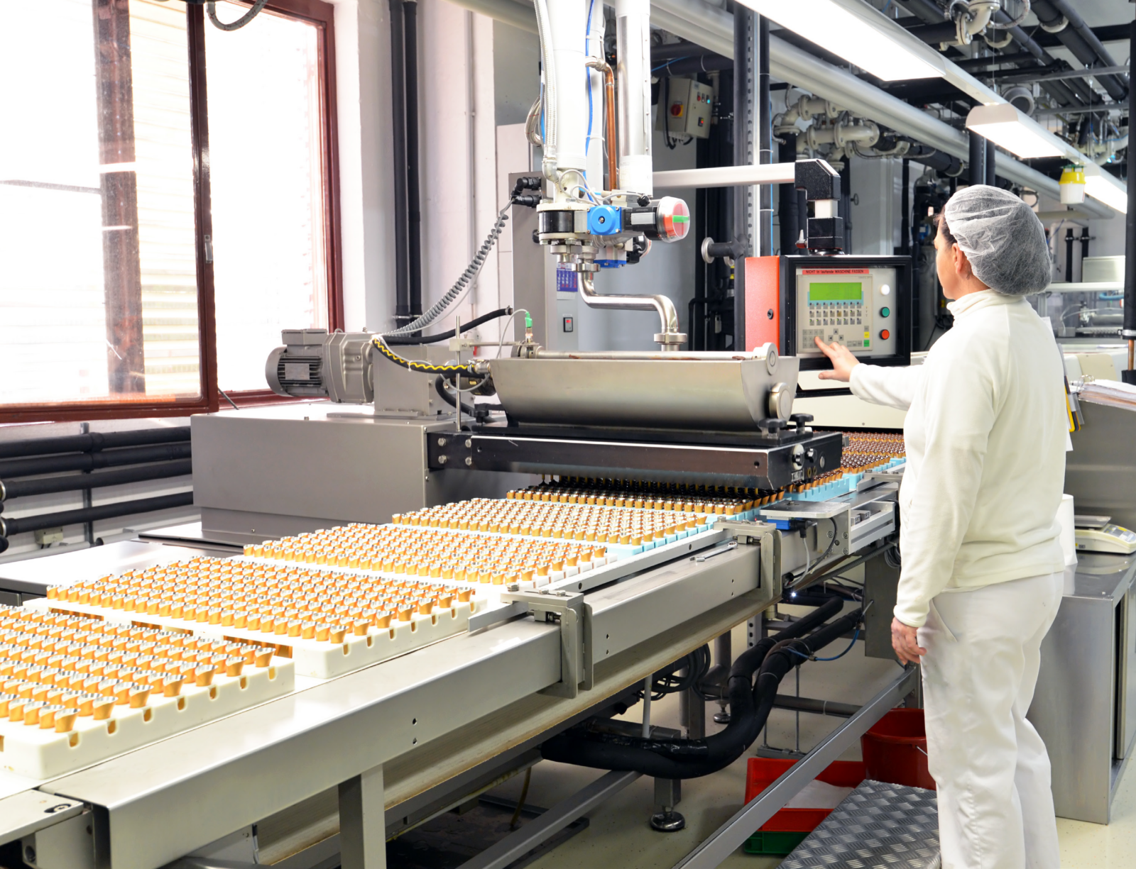 Automated production line moving rows of small containers beneath a control panel