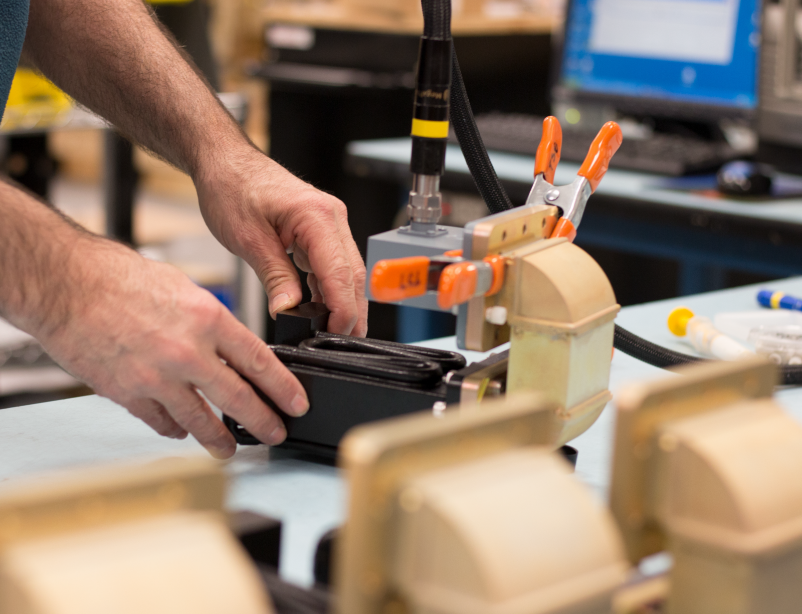 Hands positioning a small electronic device into a clamped testing or assembly fixture on a workbench